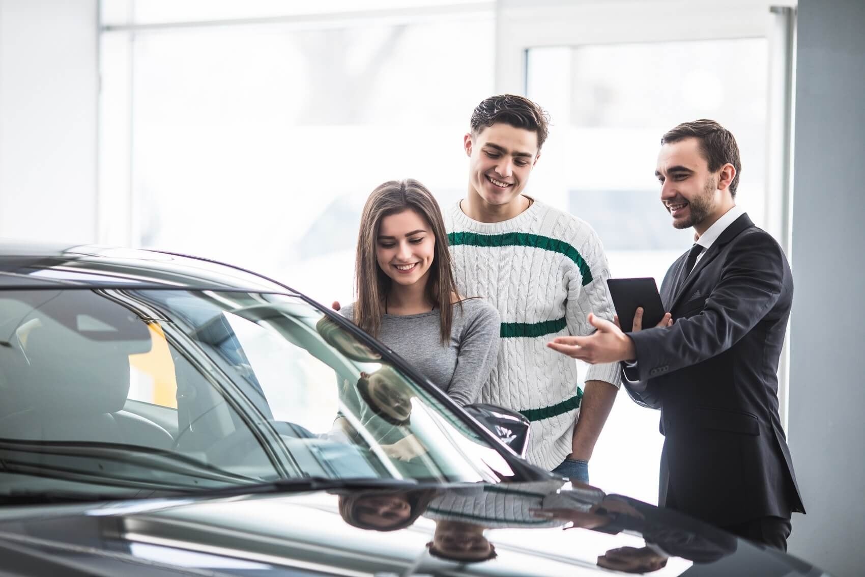 image of a young couple looking at a car with a salesman standing nect to them